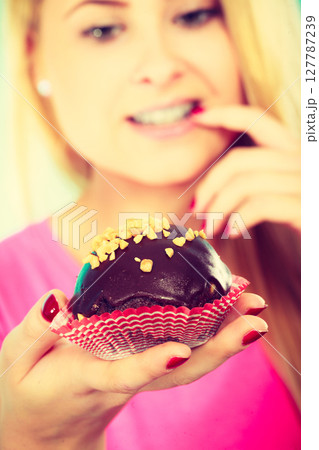Cute blonde woman thinking about eating cupcake 127787239
