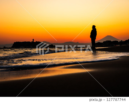 神奈川県鎌倉市、七里ヶ浜海岸の夕暮れの景色を眺める男性 127787744