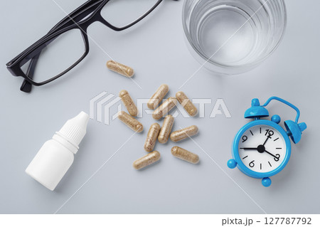 Supplement, vitamin capsule with eye glasses, eye drops and clock on table, supplement for eye health and vision 127787792