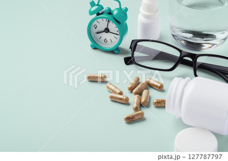 Natural vitamin, supplement spilling out of medical bottle with clock and eyeglasses on green background Natural vitamin, supplement spilling out of medical bottle with clock and eyeglasses on green background 127787797