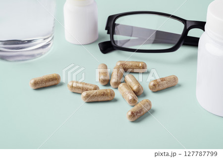 Supplement capsule with medical bottle and eyeglasses on green background, vitamin for eye health and vision concept Supplement capsule with medical bottle and eyeglasses on green background, vitamin for eye health and vision concept 127787799