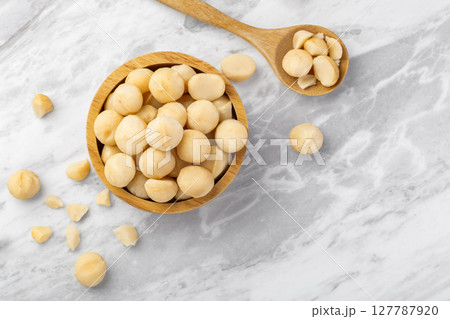 Macadamia nuts in wooden bowl with spoon and cracked macadamia on marble table background, top view Macadamia nuts in wooden bowl with spoon and cracked macadamia on marble table background, top view 127787920