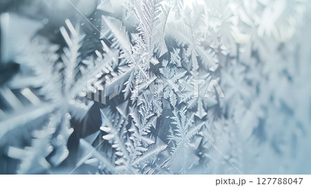 Macro shot captures intricate ice crystals on a windowpane, showcasing delicate patterns in stunning detail. 127788047