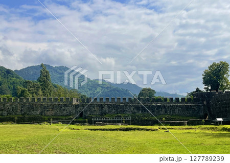 Old wall of Roman Fortress with green grass, blue sky and white clouds. Beautiful landscape 127789239