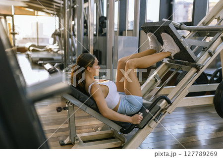 Beautiful woman sporty girl exercising using leg press machine at the gym 127789269