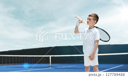 Young boy in tennis outfit holding racket and ball on blue court under clear sky. Visualizing goals 127789488