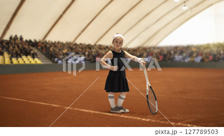 Young girl confidently posing on indoor clay tennis court with racket. Visualizing goals Young girl confidently posing on indoor clay tennis court with racket. Visualizing goals 127789503