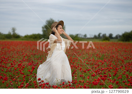 Young woman in a white dress and hat posing among summer poppies 127790029