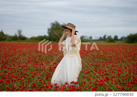 Young woman in a white dress and hat posing among summer poppies 127790030