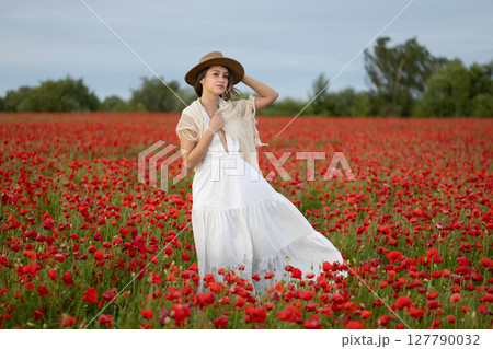 Young woman in a white dress and hat posing among summer poppies 127790032