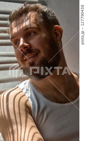 Glam shadows. Smiling man sits in partial light, shadow lines from blinds across his face. 127790438