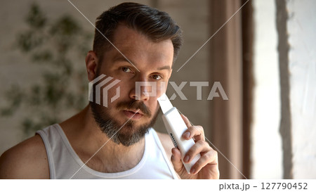 Beauty-tech. Man using facial skincare device in natural light near window Beauty-tech. Man using facial skincare device in natural light near window 127790452
