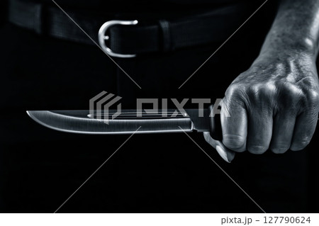 A knife in a male hand. Dark background. Dark atmosphere A knife in a male hand. Dark background. Dark atmosphere 127790624