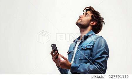 young man in denim jacket looking up while holding a smartphone 127791153