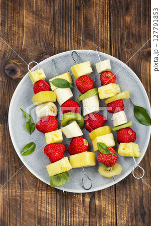 Fruits on skewers, dessert on wooden surface. Fruits on skewers, dessert on wooden surface. 127791853
