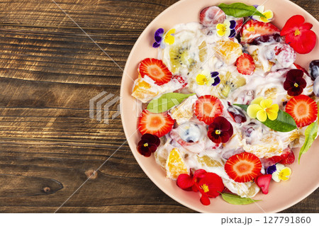 Fruit salad decorated with flowers on wooden surface. Fruit salad decorated with flowers on wooden surface. 127791860