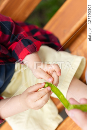 Little child eats fresh green peas which gives his mother. Selective focus, defocus. 127793505