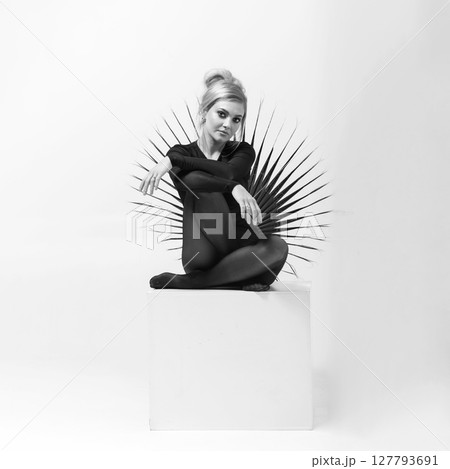 Black and white portrait of beautiful woman with tight black clothes sitting on white cube Black and white portrait of beautiful woman with tight black clothes sitting on white cube 127793691