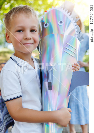 Smiling boy holds colorful shark-shaped Schultuete filled with gifts on his first day of school in Germany. Shiny cone with fins and eyes symbolizes tradition and excitement for new beginnings 127794583