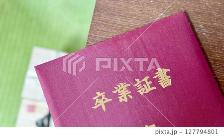 片付け中にテーブルに置いた赤い表紙の卒業証書 片付け中にテーブルに置いた赤い表紙の卒業証書 127794801
