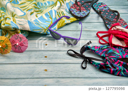 Swimwear, sunglasses, flip flops and beach towel with a tropical print on a wooden table. 127795098