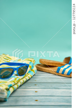 Blue sunglasses, sandals and beach towel, on a wooden table and a green background. Blue sunglasses, sandals and beach towel, on a wooden table and a green background. 127795114