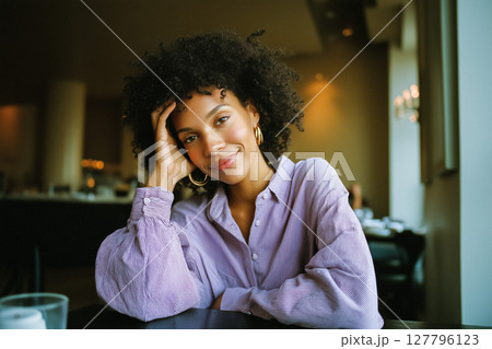 A woman with curly hair is sitting at a table with a purple shirt on A woman with curly hair is sitting at a table with a purple shirt on 127796123