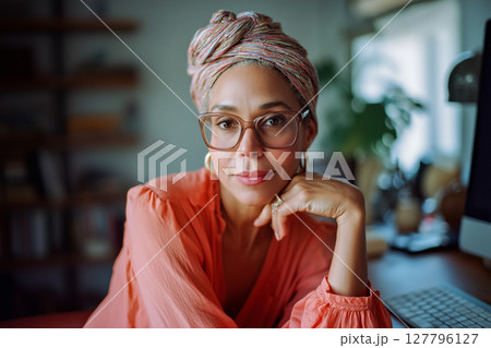 A woman wearing glasses and a pink shirt is sitting at a desk with a computer 127796127