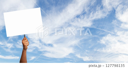 Hand holding a blank sign against a blue sky with fluffy clouds during daylight 127798135