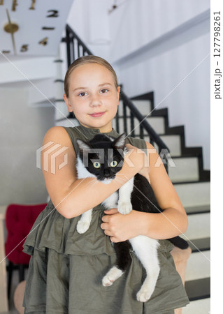 Lovely child girl holding playful furry cat pet companion standing indoor Lovely child girl holding playful furry cat pet companion standing indoor 127798261