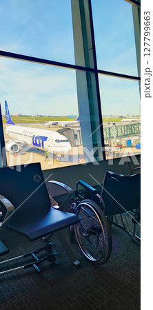 View from the airport terminal with a wheelchair and crutches in the foreground. Concept of inclusiveness and assistance at the airport for disabled people, pensioners 127799663