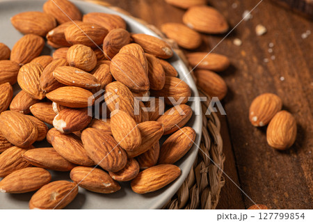 Almonds nuts on a plate placed on a rustic wooden board. Delicious sweet almonds on the wooden table, roasted almond nut for healthy food and snack 127799854