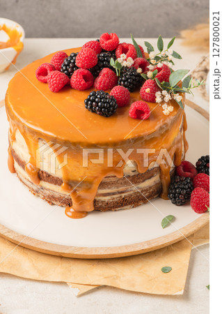 Delicious chocolate cake topped with mascarpone cream and salted caramel. Decorated with red fruits. Light background Delicious chocolate cake topped with mascarpone cream and salted caramel. Decorated with red fruits. Light background 127800021