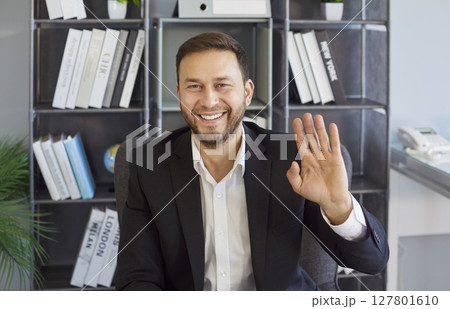 Businessman waving hello, interacting on video call with friendly gesture and open smile, attention Businessman waving hello, interacting on video call with friendly gesture and open smile, attention 127801610
