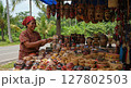 Indonesian Woman Selling Traditional Handcrafted Masks and Woven Baskets at Outdoor Market 127802503