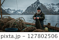 Nordic Fisherman Mending Nets on a Boat with Snowy Mountain Backdrop in Norway 127802506