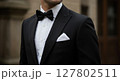 Close-Up of Elegant Man Wearing Black Tuxedo with Bow Tie and Pocket Square Outdoors 127802511