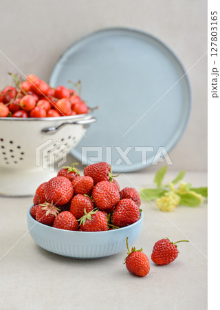 Ripe strawberries in a blue bowl and a white enamel colander full of sweet cherries 127803165