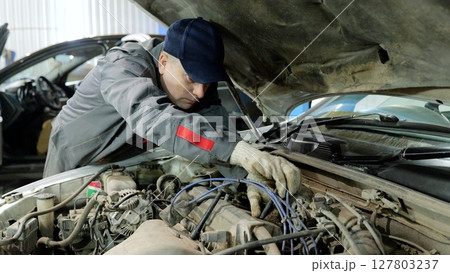 Skilled automotive technician wearing protective gloves, inspecting engine components and diagnosing mechanical problems in well equipped repair workshop 127803237