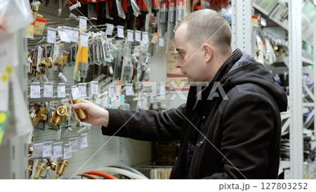 Professional plumber examining brass faucet components at hardware store, selecting precise parts for intricate plumbing repair and installation work 127803252