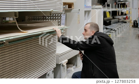 Construction worker checking drywall sheets at hardware store, comparing sizes and quality for renovation project, selecting precise building materials with professional attention Construction worker checking drywall sheets at hardware store, comparing sizes and quality for renovation project, selecting precise building materials with professional attention 127803258