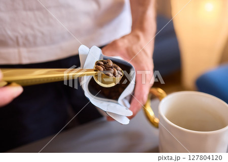 Pouring freshly ground coffee beans into a measuring cup for a perfect morning brew Pouring freshly ground coffee beans into a measuring cup for a perfect morning brew 127804120