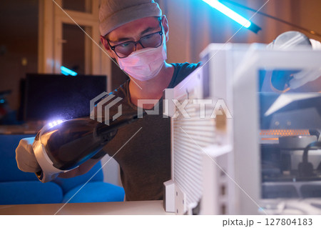A man cleans a computer case with a vacuum in a bright room, stressing workspace tidiness A man cleans a computer case with a vacuum in a bright room, stressing workspace tidiness 127804183