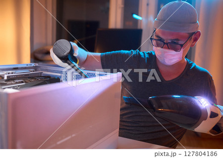 A man cleans a computer case with a vacuum in a bright room, stressing workspace tidiness 127804186