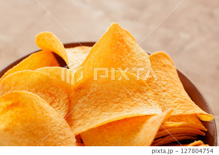 Stacked Golden Potato Chips in Bowl on Beige Background Close-Up 127804754