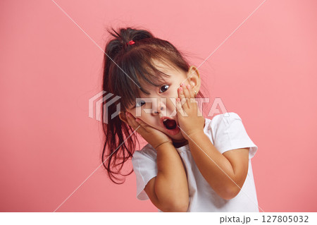 Headshot of stupefied little girl keeps hands on cheeks standing over pink isolated background. Surprised asian child expresses shock. Headshot of stupefied little girl keeps hands on cheeks standing over pink isolated background. Surprised asian child expresses shock. 127805032