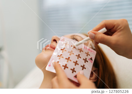 Professional beautician applying eyebrow stencil, creating symmetrical makeup design with precision cosmetic technique in modern beauty clinic. Concept of rejuvenating skin, preventing aging. 127805226