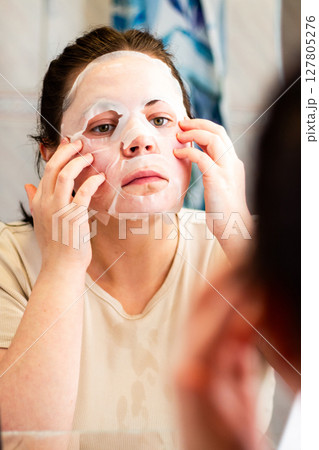Evening skincare routine. Female applying nourishing face mask. Late night face care. Reflection in bathroom mirror. Dermatology concept. Evening skincare routine. Female applying nourishing face mask. Late night face care. Reflection in bathroom mirror. Dermatology concept. 127805276