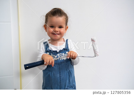 Little girl doing home renovation, painting a wall in the living room with a roller brush Little girl doing home renovation, painting a wall in the living room with a roller brush 127805356