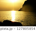 Stunning golden sunset over the sea in Calabria, Italy, with soft sunlight reflecting on the water and the curved silhouette of mountain cliffs in the distance. Serene coastal landscape with warm 127805854
